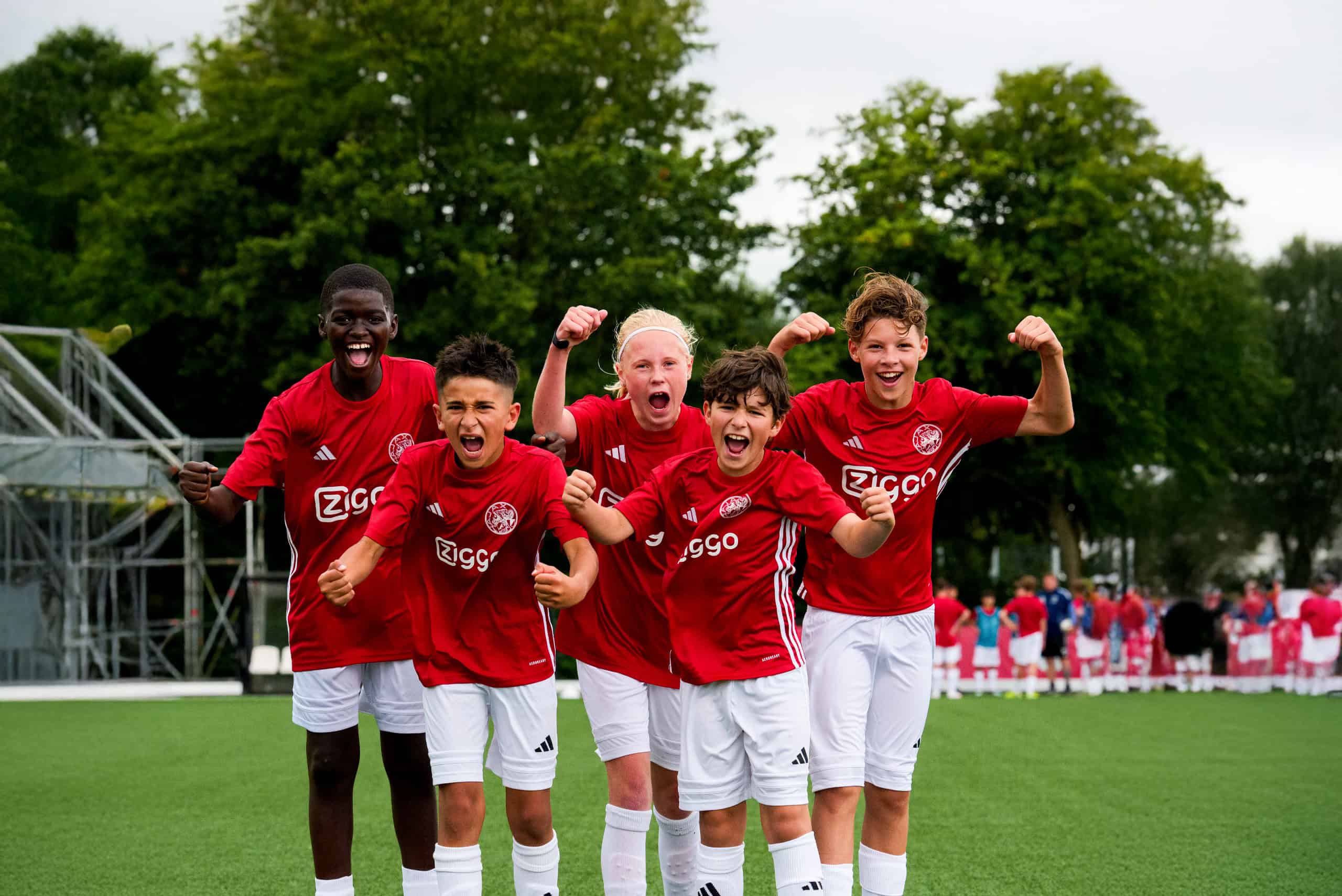 Energieke jeugdvoetballers in Ajax-shirt vieren overwinning op het veld.