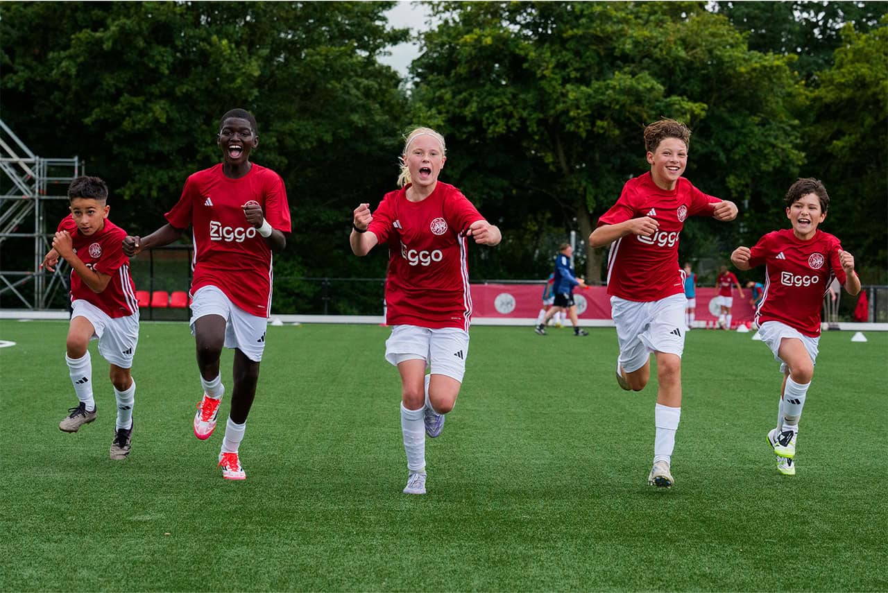 Energieke jeugdvoetballers in Ajax-shirt vieren overwinning op het veld.
