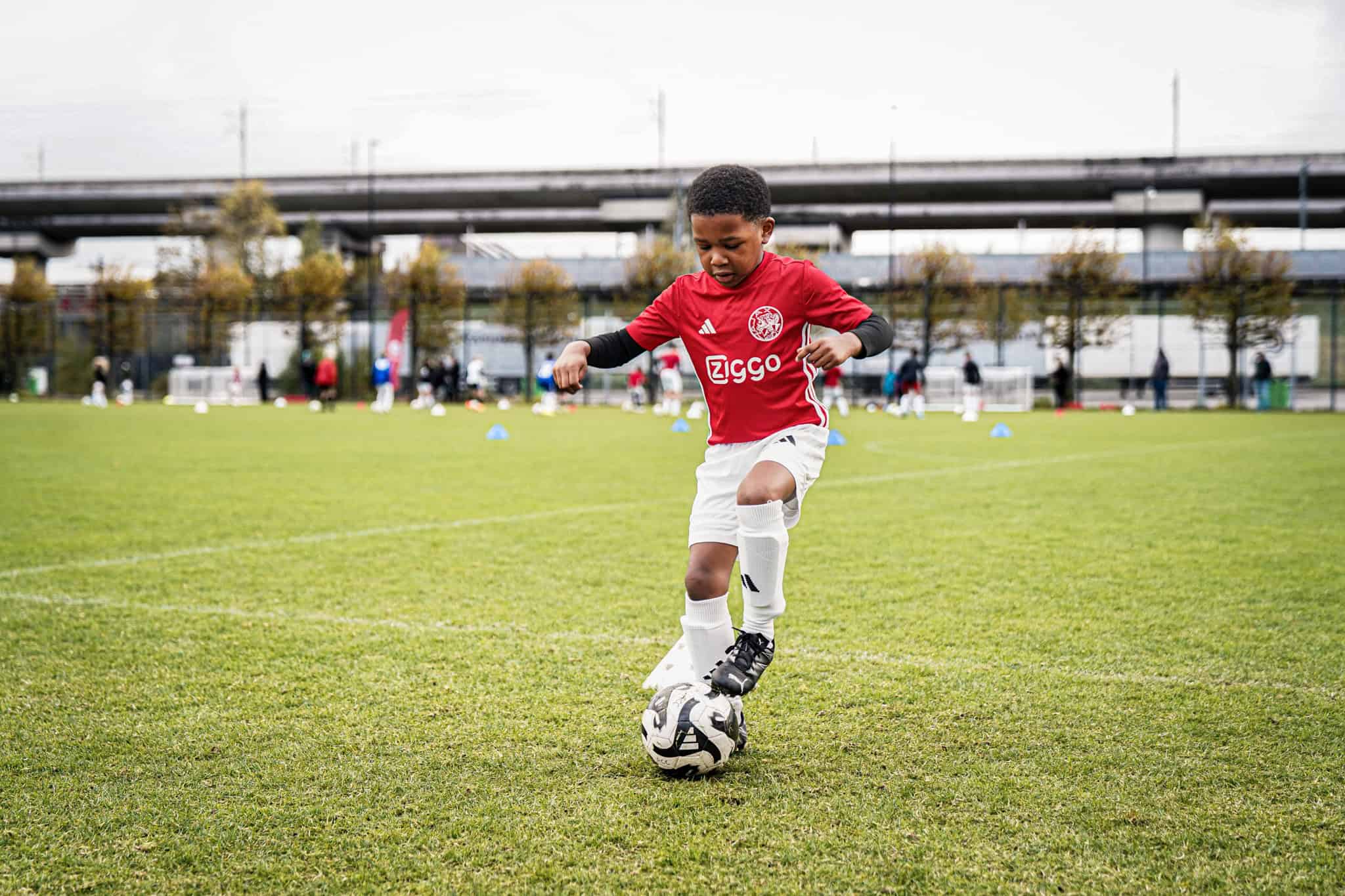 Jonge speler traint met voetbal op een veld tijdens Ajax Camps & Clinics.